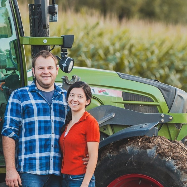 KI generiert: Ein Paar steht lächelnd vor einem Traktor auf einem Feld.
