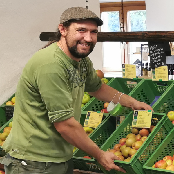 KI generiert: Ein Mann sortiert Äpfel in grünen Kisten. Text: "Äpfel aus unseren ungespritzten Streuobstwiesen 4,50€/kg".